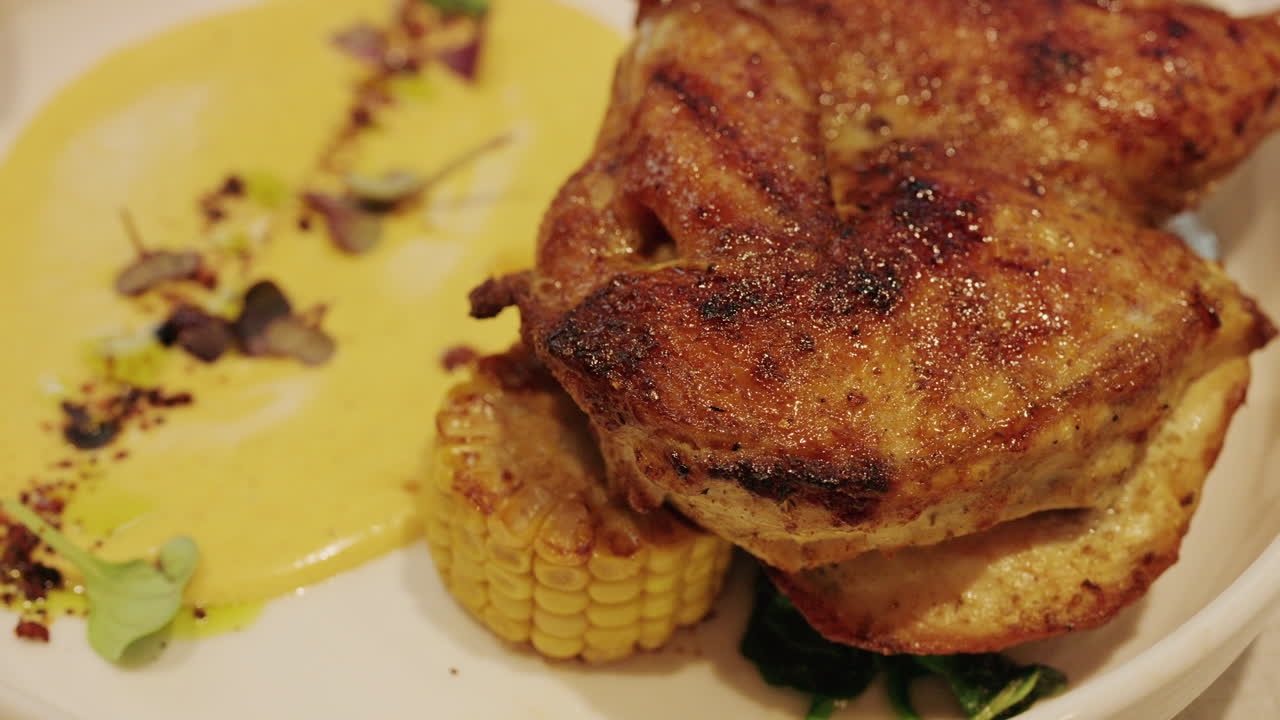 Primo piano di una coscia di pollo alla griglia servita con salsa cremosa, mais e verdure.