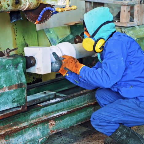 worker is polishing stone on the industrial machine. laborer in working clothes grinding rock on the factory background.