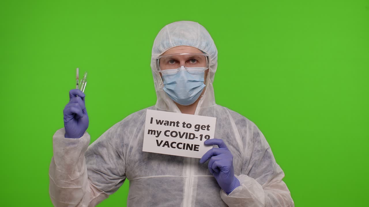 의료복을 입은 남자가 주사기를 들고 '코로나19 예방 접종을 받고 싶다'는 표지판을 들고 있다.