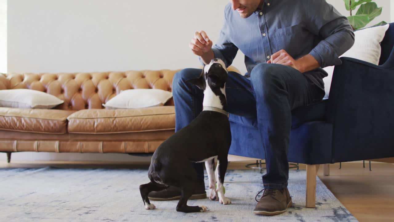 Happy caucasian man training and feeding his dog at home