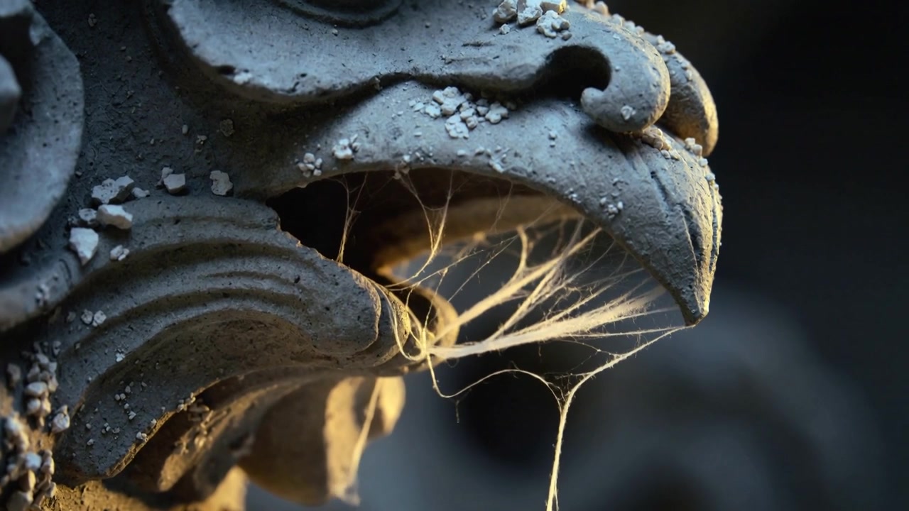 Luce dell'ora d'oro che contorna e rivela il becco di un gargoyle in pietra consumata sulla linea del tetto, con fili di seta.