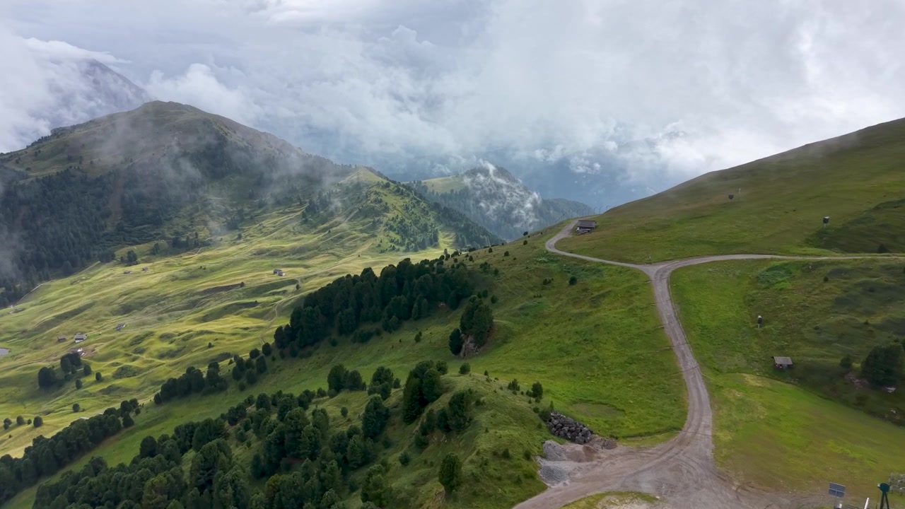 Vista drone dei dolci prati alpini della Seceda con gli edifici della stazione di montagna sotto nuvole drammatiche nelle Dolomiti, Italia.