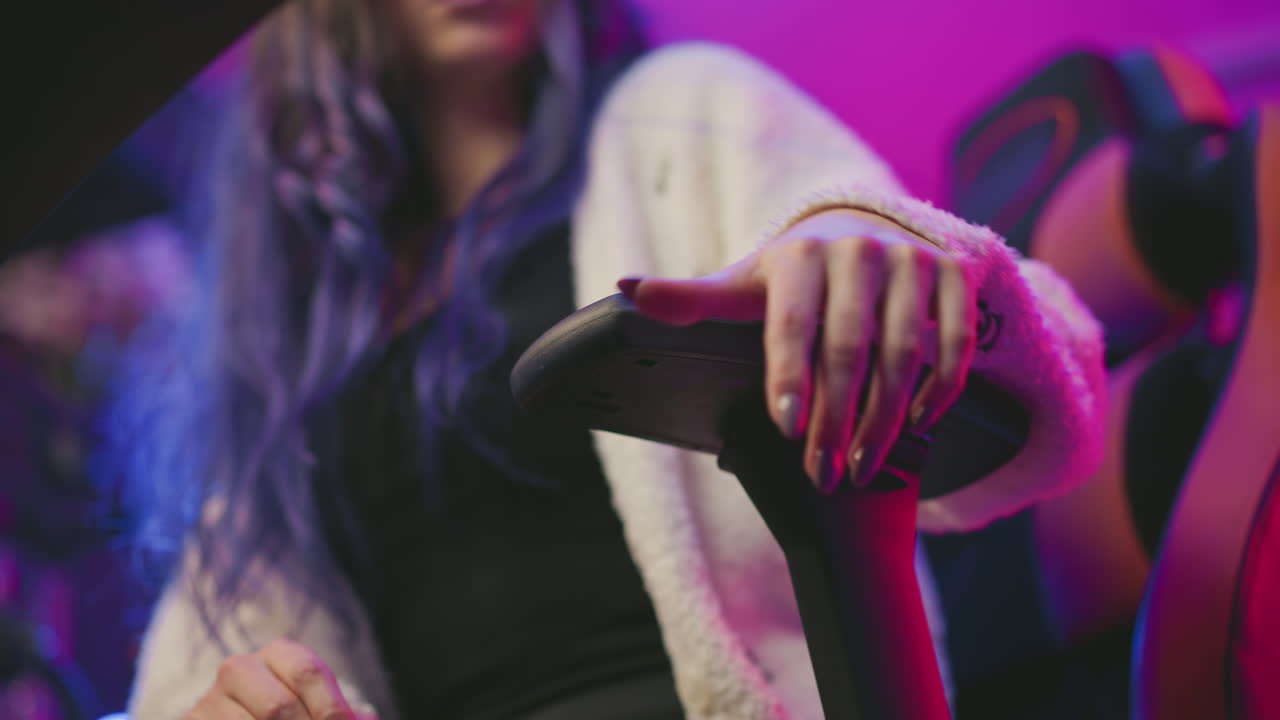 Upward angle showing woman adjusting armrest of gaming chair while resting hand on it and turning slightly, wearing fluffy sweater in vibrant studio with pink and purple lights and blur background