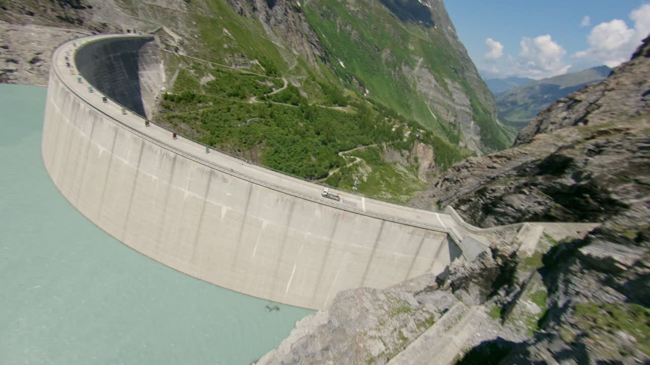 Stunning FPV and drone shots soaring through the Swiss Alps, capturing the Mauvoisin Dam and its majestic waterfall on a clear, sunny summer day.