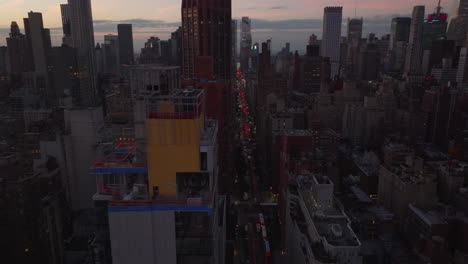 Fly-between-high-rise-buildings-in-city-at-twilight.-Long-straight-avenue-with-traffic.-Manhattan,-New-York-City,-USA