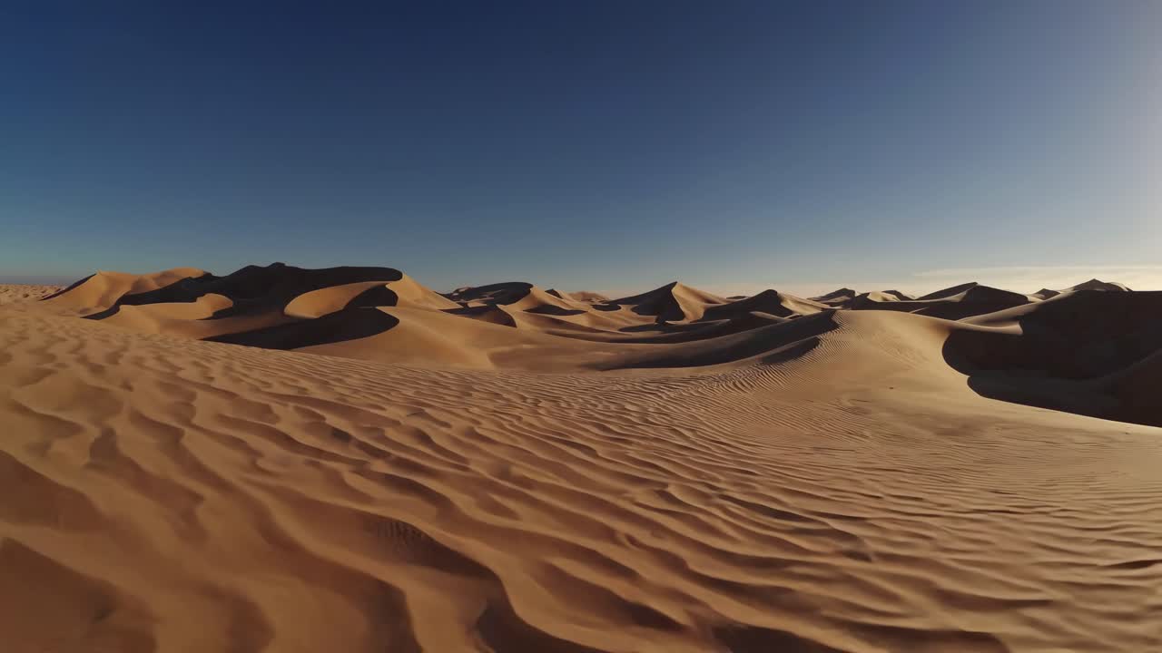 Aerial video of vast desert dunes under a clear blue sky, showcasing sweeping sand patterns