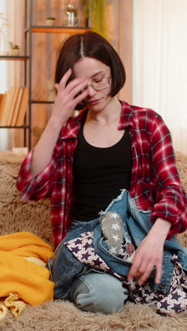 young woman sorting clothes on home sofa thoughtfully deciding what to keep and what to give away