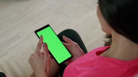 vista trasera de una mujer sosteniendo un teléfono inteligente de pantalla verde con llave de croma viendo contenido y tocando o deslizando.
