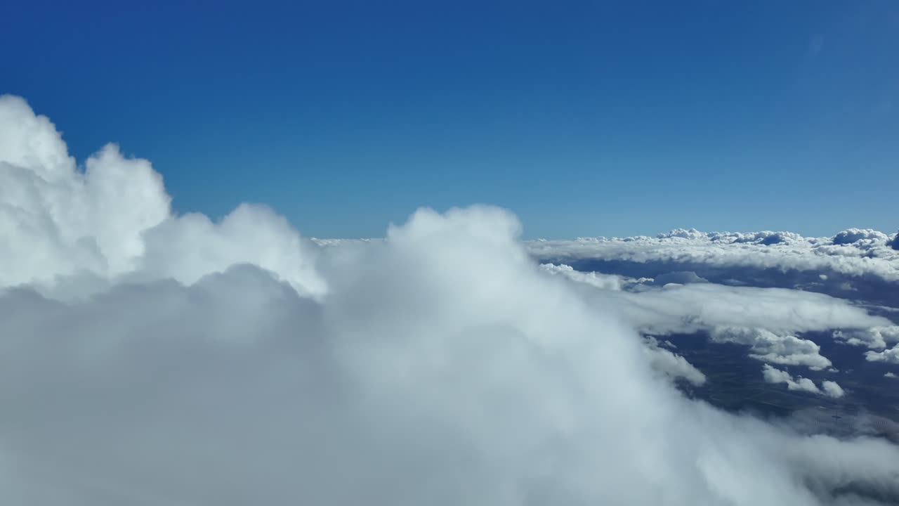 An aerial view through the pilot’s eyes in a real time flight over the top of towering storm clouds under a deep blue sky. Ultra-realistic 4K
