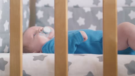 little boy sucks dummy lying in comfortable baby bed