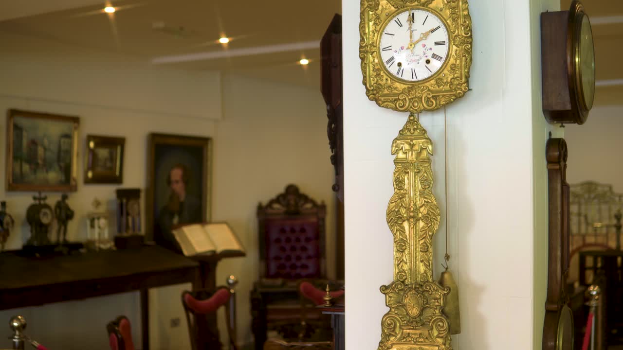 золотые винтажные старомодные часы висят на столбе в антикварном магазине с множеством различных предметов на заднем плане замедленная съемка