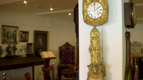 Golden-vintage-old-fashioned-clocks-hanging-on-a-pillar-inside-antique-shop-with-many-different-objects-at-the-backround-slow-motion