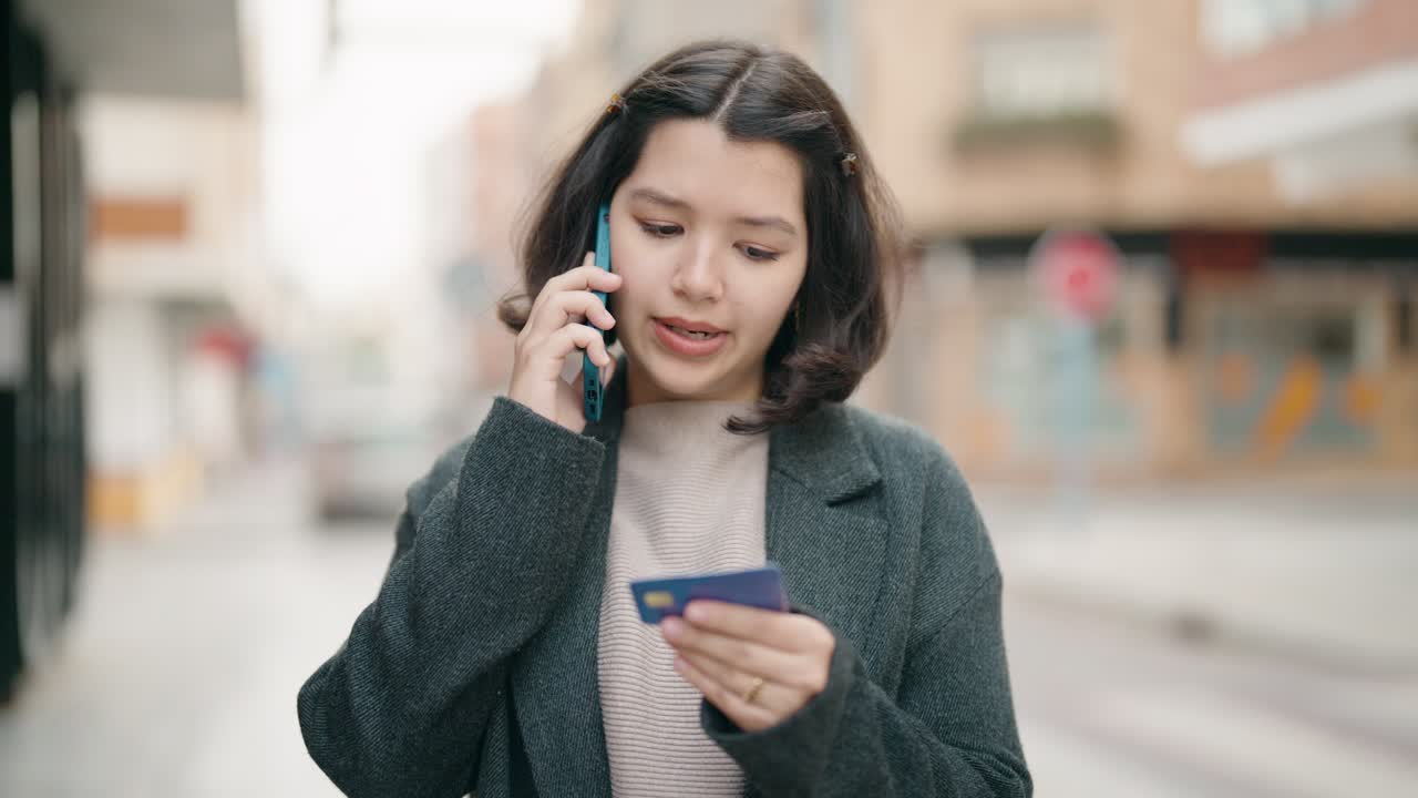 joven hispana hablando en el teléfono inteligente y usando tarjeta de crédito en la calle