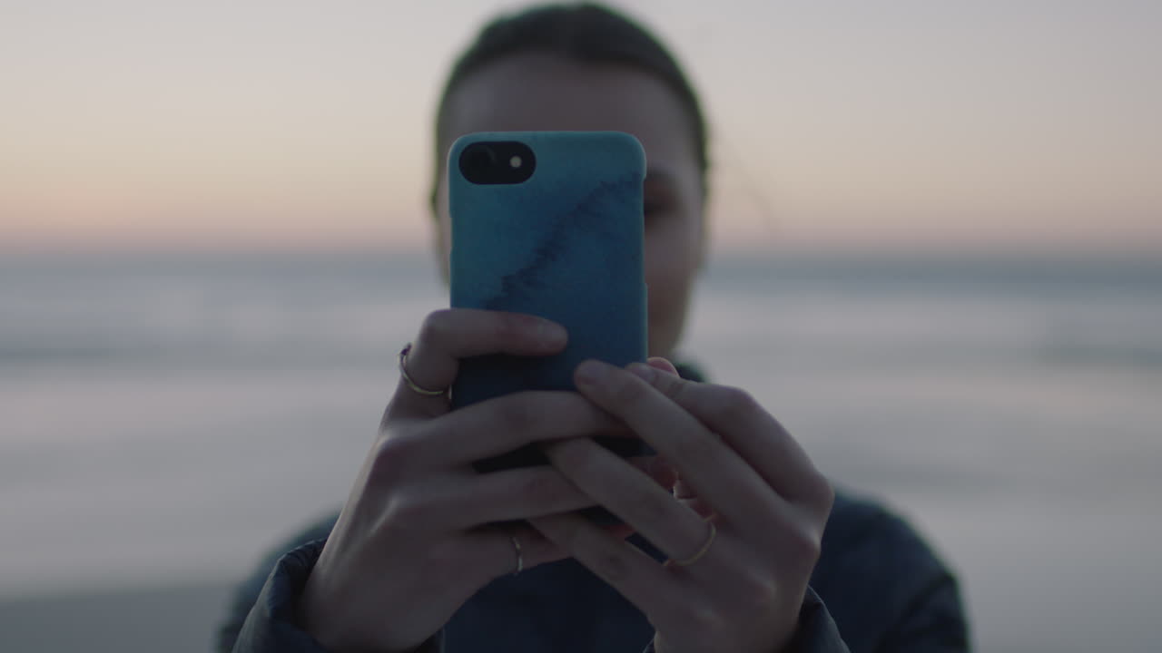 retrato en primer plano de una mujer joven tomando una foto utilizando la tecnología de cámara móvil de un teléfono inteligente en una playa tranquila al atardecer