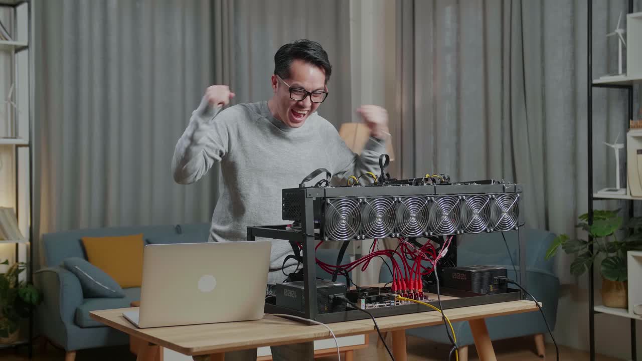 행복한 아시아 남자가 암호화폐 채굴을 위한 채굴 기지에서 성공을 축하하고 있습니다.