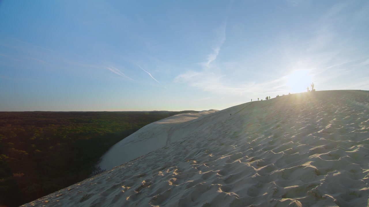 Tramonto invernale su dune di sabbia dorata con bagliore solare e silhouette