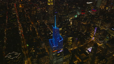 Vista-De-ángulo-Alto-De-La-Parte-Superior-Iluminada-En-Azul-De-Un-Rascacielos-Alto-De-Vanderbilt.-Ciudad-De-Noche-En-Segundo-Plano.-Manhattan,-Ciudad-De-Nueva-York,-Estados-Unidos