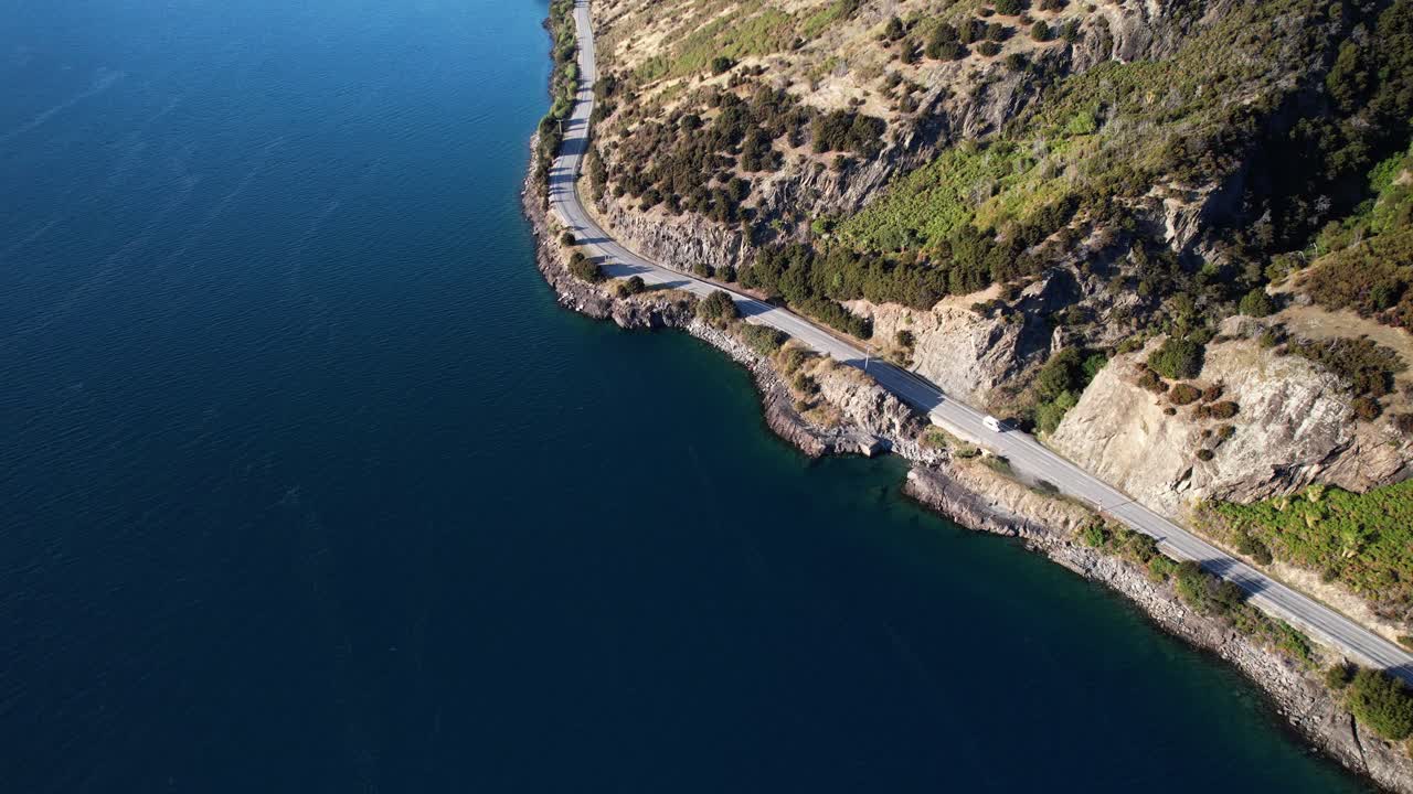 Coastal Road Winding Through Rugged Terrain On Shore Of Lake Hawea On South Island, Otago, NZ. aerial shot
