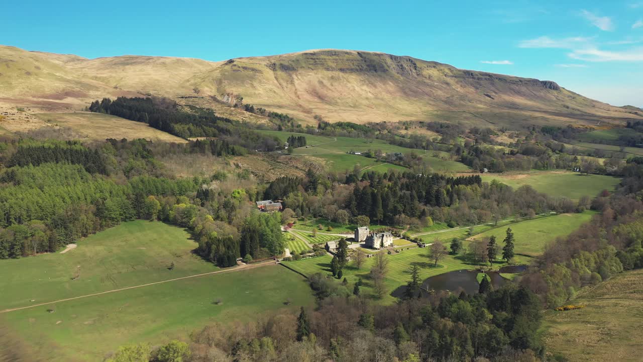 Aerial view of a historic castle estate nestled in a lush green valley with mountains