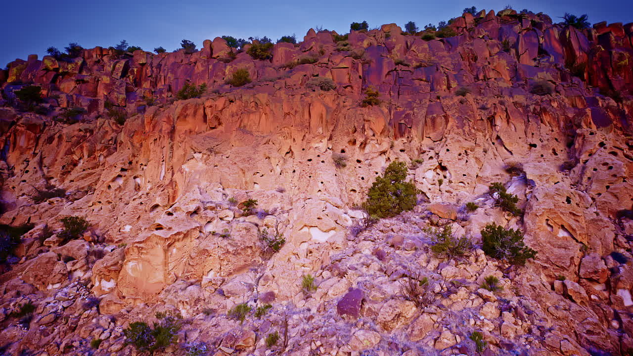 Riprese con drone che si allontanano da una mesa desertica, svelando scogliere dai colori intensi sotto cieli al tramonto.