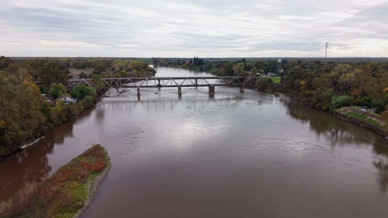 Aerial push in shot captures the Tehama Railroad Bridge rising over the water, its weathered structure set against the peaceful greenery of Mill Creek Park