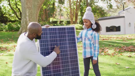 video de un feliz padre afroamericano explicando el panel solar a su hija en el jardín de otoño