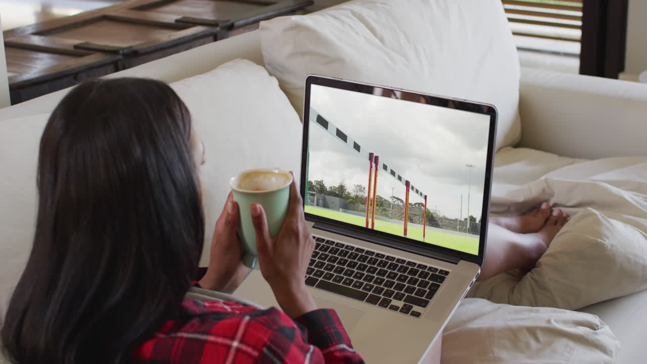 Composite of woman sitting at home holding coffee watching athletics running event on laptop