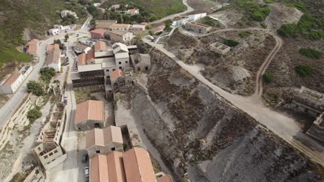 Aerial-backward-shot-of-the-abandoned-buildings-and-heaps-of-the-former-silver-mines-in-Argentiera,-Italy---end-of-the-natural-resources-concept