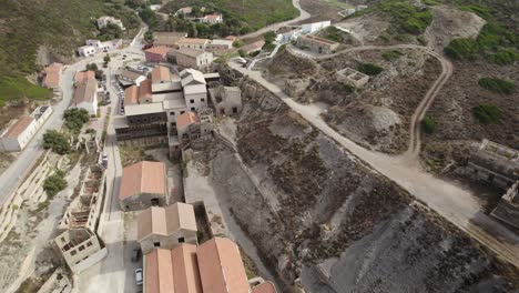 toma aérea hacia atrás de los edificios abandonados y montones de las antiguas minas de plata en argentiera, italia - fin del concepto de recursos naturales