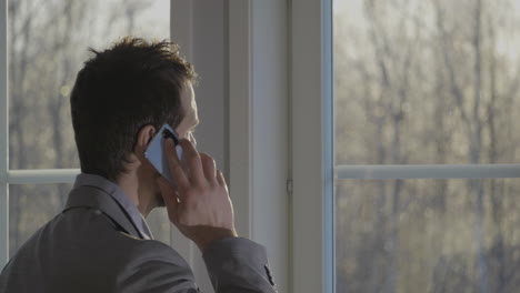 Hombre-Caucásico-Mirando-Por-La-Ventana-Y-Hablando-Por-Teléfono-Para-Trabajar