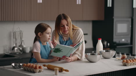madre feliz y la niña están leyendo el recibo de la masa en el libro de cocina madre e hija están cocinando en la cocina de casa