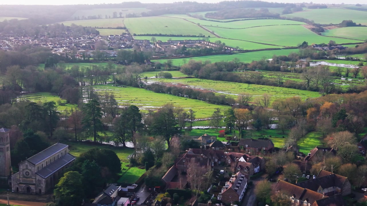 Aerial drone footage of a village with a large church waterlogged meadows a river and surrounding fields in winter