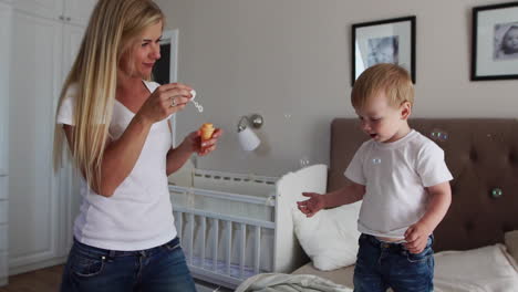 Caring-mother-plays-son-looking-at-soap-bubbles,-the-boy-is-happy-jumping-on-the-bed