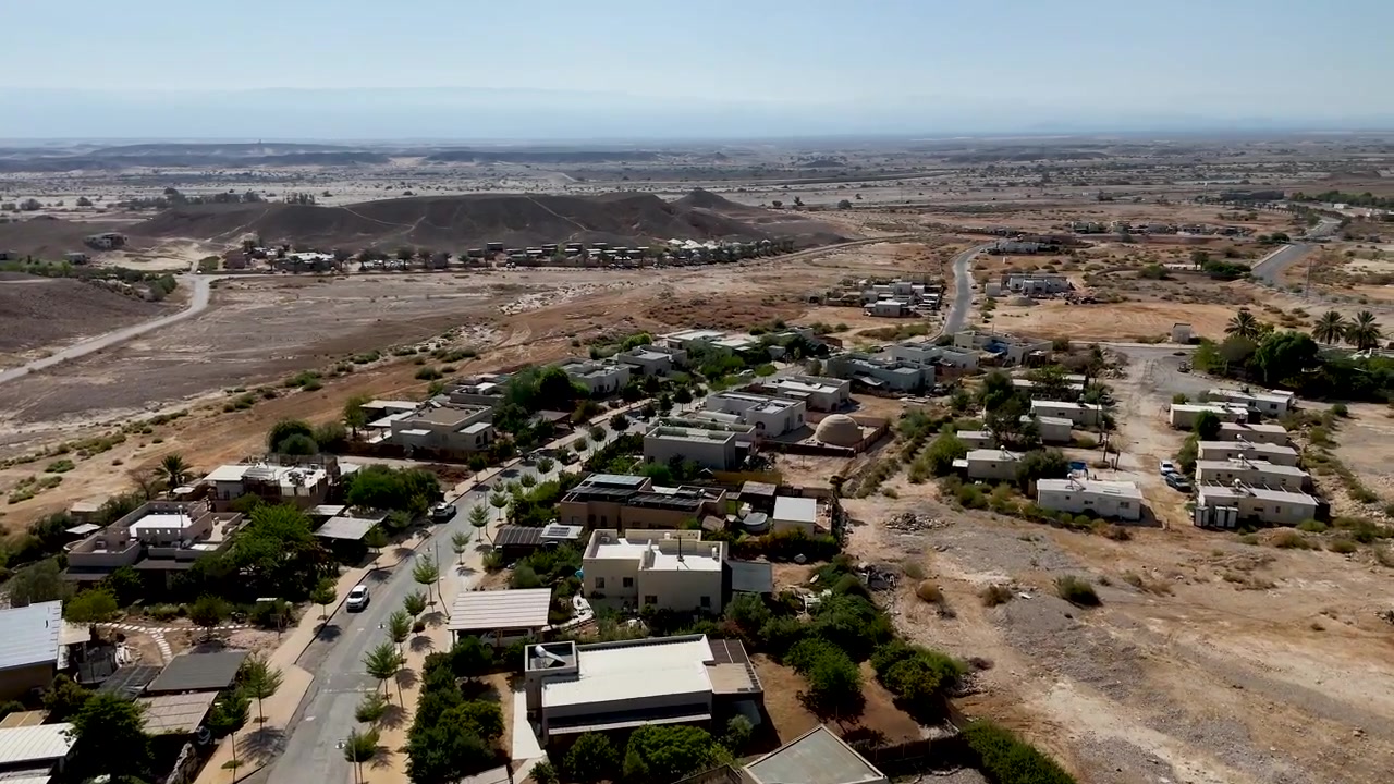 4K 60fps drone footage flying eastward from the remote desert toward Zukim, Israel, crossing over the village and revealing its homes, rugged surroundings and expansive Arava landscape