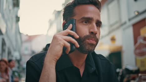 hombre barbudo bebiendo un vaso de vino llamando en un café callejero de cerca. hombre hablando por teléfono