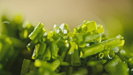 close macro shot of fresh chopped chives laying on a wooden cutting board, then water is sprayed on it