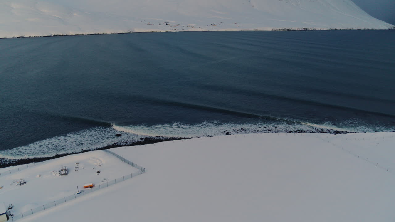 Icy Arctic ocean meets Icelandic coastline covered in snow, tranquil winter seascape aerial establishing