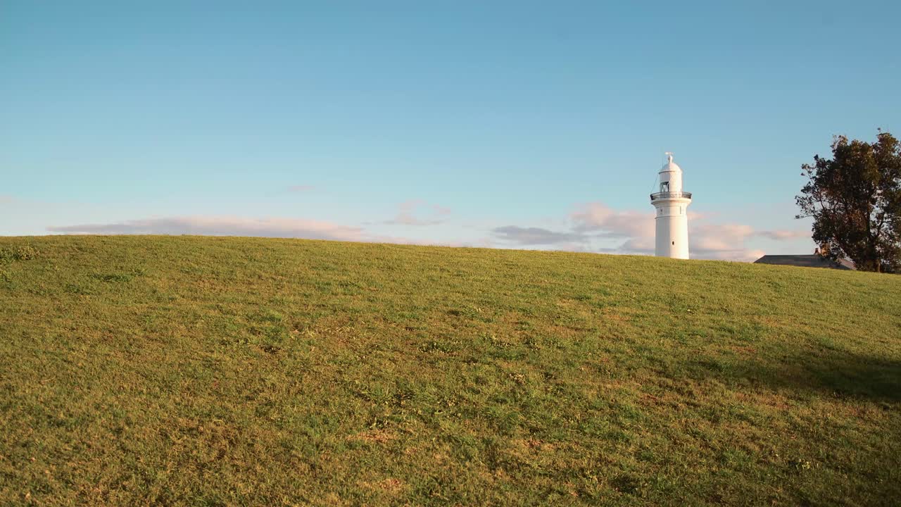 белый маяк появляется над зеленым холмом на закате