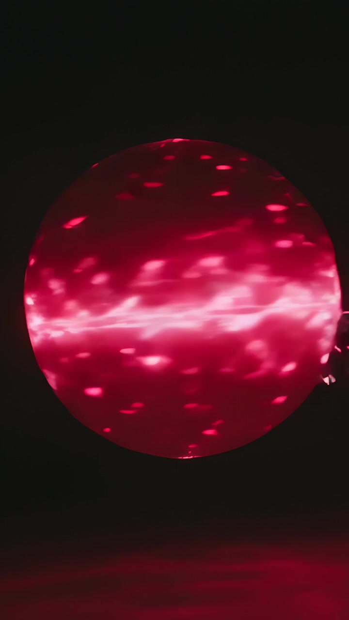 Vídeo vertical: Enviando faíscas brilhantes, orbe vermelho luminoso flutuando sobre plano escuro, faixa central ondulante.