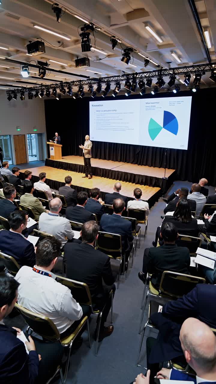 Engaging speaker presenting innovative ideas to a large audience of business professionals during a corporate conference, fostering collaboration and knowledge sharing in the business world