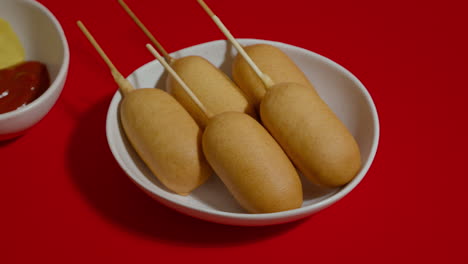 Close-up-view-of-white-plate-with-corn-dogs-shotting-on-red-background.