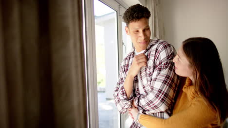 happy diverse couple looking through window and embracing at home, copy space, in slow motion