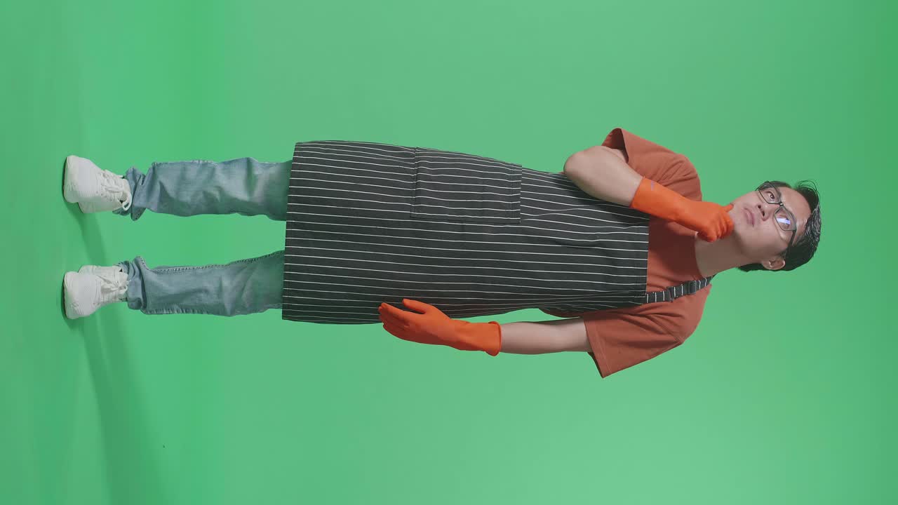 무언가에 대해 생각하고 주위를 둘러보며 녹색 스크린 스튜디오에서 지표손가락을 들어 올리는 아시아 남성 집사.