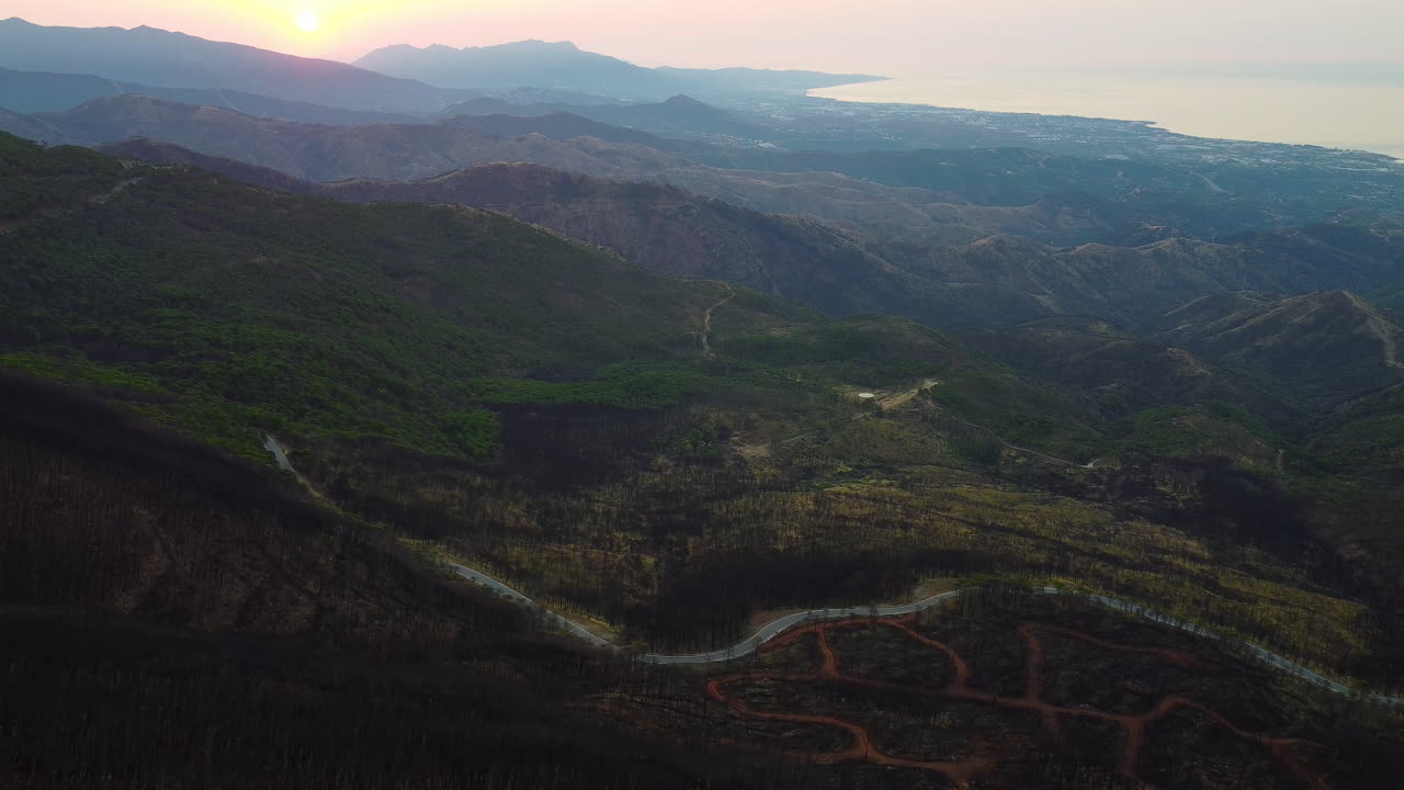 un avión no tripulado vuela sobre los restos quemados de un bosque cerca de una carretera de montaña en pico de los reales, estepona, españa