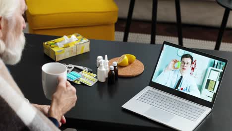 primer plano de un hombre enfermo con una taza de bebida caliente sentado en la habitación y hablando en video en una laptop con el médico