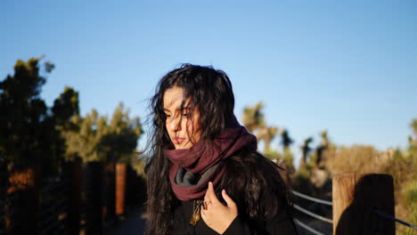 a beautiful girl with long black hair adjusting her red scarf in slow motion on a hike in autumn desert