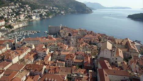 aerial footage of old town in dubrovnik, the camera passes over dubrovnik cathedral and port showing the distant coastline