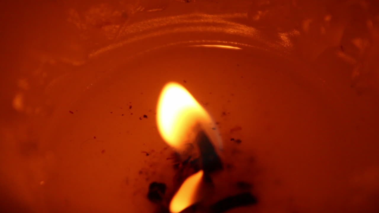 vista muy cercana de una vela naranja, roja con cera derretida dentro de la caja, desdibujándose hasta que se convierte en una bombilla de luz en movimiento abstracto