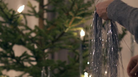 Woman-preparing-for-X-mas-celebrations,-hanging-silver-decorations-in-Christmas-tree-on-the-Night-Before-Christmas