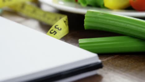 ensalada de verduras en un plato con cinta de medición y cuaderno en espiral en la mesa